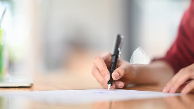 Closeup Female Signing Document Focus On Her Hand Holding Pen Putting Signature On Official Paper.