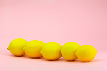Yellow lemons laid diagonally on a pink background