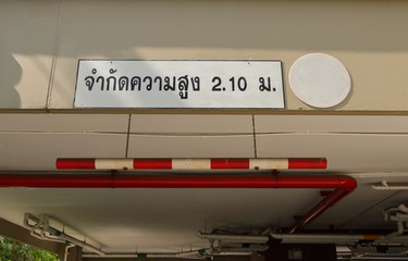 Closeup car height limit sign made from PVC pipe painted with red and white, hanging from ceiling by chains, the Thai language means limit height 2.10 m 