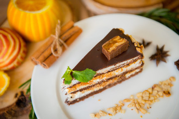 A piece of chocolate cake in a white plate against the background of oranges and honey in the restaurant's interiors. Restaurant menu.