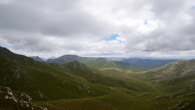 Beautiful panning time lapse of cloudscape soaring over green valley between mountain hilltops, sunlight patches trailing along the ground.