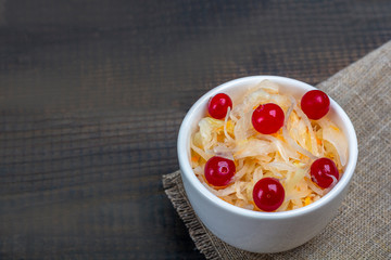 Sauerkraut or fermented cabbage with cranberries in a bowl on rustic wooden background. The concept of proper nutrition and healthy eating. Organic and vegetarian food. Close up, copy space for text