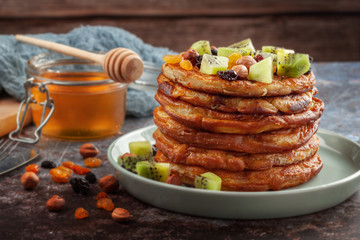 On the table is a dish with pancakes, honey, kiwi, nuts and raisins.