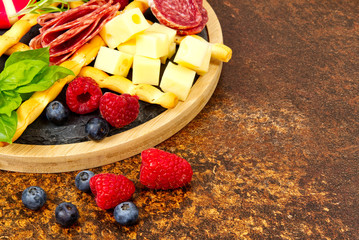 Meat and cheese plate antipasti snack with Prosciutto ham, Parmesan, Blue cheese, Cantaloupe melon and Olives on olive wood serving board on dark stone background