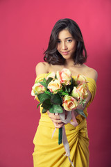 Beautiful young woman wearing yellow elegant dress standing holding roses flowers and smiling on pink background Isolated, Thailand.