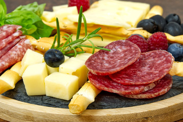 Meat and cheese plate antipasti snack with Prosciutto ham, Parmesan, Blue cheese, Cantaloupe melon and Olives on olive wood serving board on dark stone background