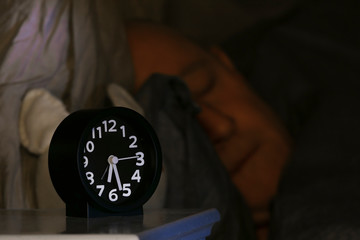 An alarm clock on a bedside table and a teddy bear.