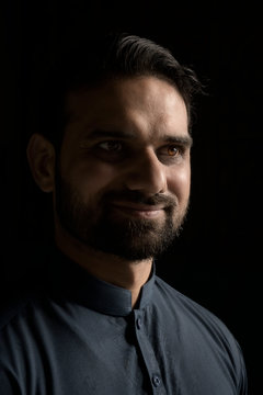 Man with beard and brown eyes color standing with light and shadow on his face smiling and looking on black background, Bahrain.