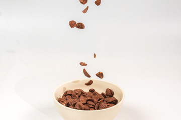 Chocolate corn flakes falling to the white bowl isolated on white. Motion.