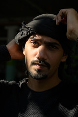 Young middle east man with beard holding turban looking with sunlight shine on his eyes on black background, Bahrain.