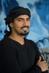 Handsome middle east man with beard wearing black shirt and traditional turban on head smiling on colorful background