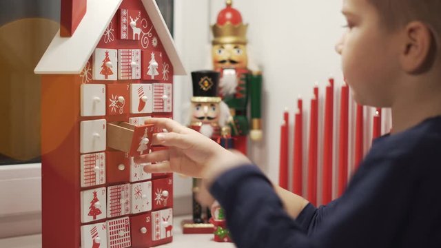 Happy Little Boy Takes Sweet From Advent Calendar House Form With Christmas Nutcrackers in Background. Traditional Christmas Calendar for Kids