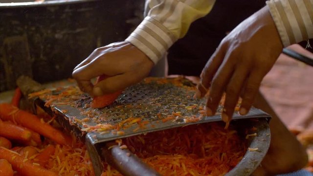 Closeup shot of an Indian man grating the carrot to prepare Gajar Ka Halwa (Famous Sweet in India). A cook preparing carrots to make the sweet dish of carrots for the gathering at the wedding - Ind...