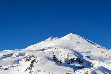 Fototapeta na wymiar Two snow-white peaks of the mountain Elbrus against a clear cloudless blue sky 