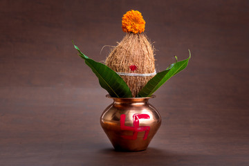 Copper kalash with coconut and mango leaf with floral decoration on a wooden background. essential...