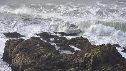 Strong waves crashing onto rocks on an ocean coastline.