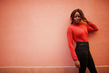 Portrait of a curly haired african woman wearing fashionable red turtleneck posing against rose...
