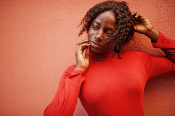 Portrait of a curly haired african woman wearing fashionable red turtleneck posing against rose...