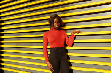 Portrait of a curly haired african woman wearing fashionable red turtleneck posing against yellow...