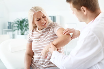 Doctor examining mature woman with joint pain in clinic