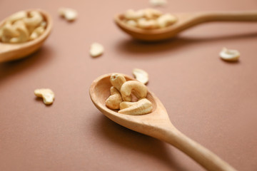 Fototapeta na wymiar Spoons with tasty cashew nuts on color background