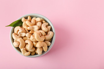 Bowl with tasty cashew nuts on color background
