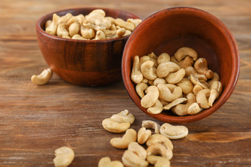Bowls with tasty cashew nuts on wooden background