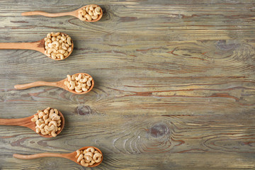 Spoons with tasty cashew nuts on wooden background