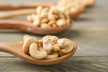 Spoons with tasty cashew nuts on wooden background, closeup