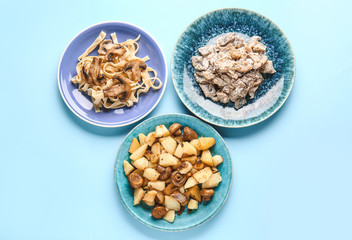 Plates with different mushrooms dishes on color background