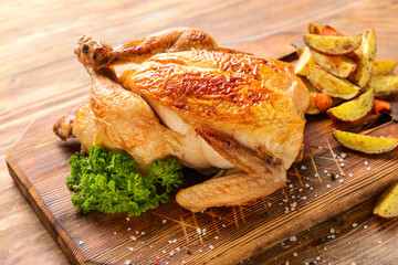 Board with baked chicken and potato on wooden table