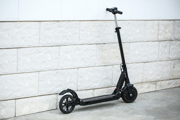Modern electric kick scooter near white brick wall © Pixel-Shot
