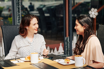 Smiling pretty female friends meeting in outdoor cafe to have some coffee and discuss news and gossips
