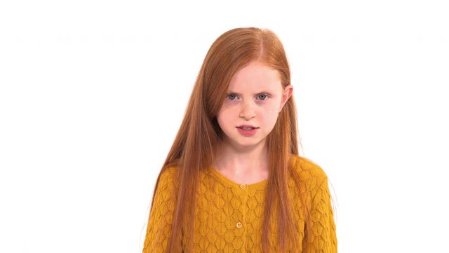 Naughty bad mannered little girl with long red hair and freckles makes very angry grumpy face at camera