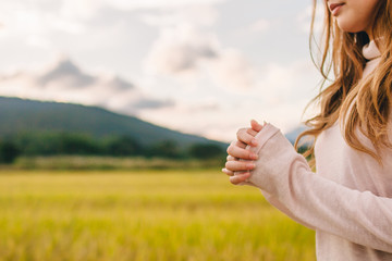 A young woman shows the symbol of prayer to God for the blessings of the Lord to find good things with faith in the sacredness and power of God on the blurred background of nature in the morning.