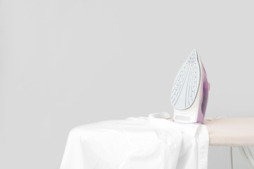 Iron and clean clothes on board against grey background