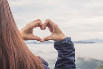Naklejka na ściany i meble The girl raises her hand to show a meaningful heart-shaped symbol. Tell her that I love you on a blurred background of nature. The concept of showing symbols to tell love Lover on valentine's day