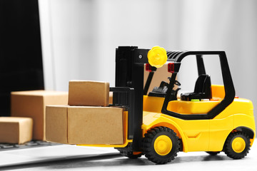 Toy forklift with boxes near laptop on table. Logistics and wholesale concept