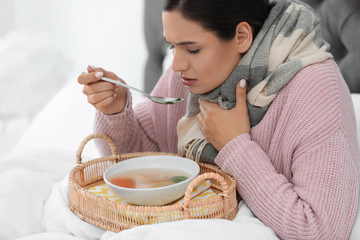 Fototapeta na wymiar Sick young woman eating soup to cure flu in bed at home