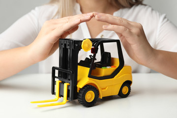 Woman covering toy forklift at white table, closeup. Logistics and wholesale concept