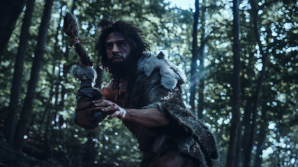 Portrait of Primeval Caveman Wearing Animal Skin and Fur Hunting with a Stone Tipped Spear in the Prehistoric Forest. Prehistoric Neanderthal Hunter Ready to Throw Spear in the Jungle