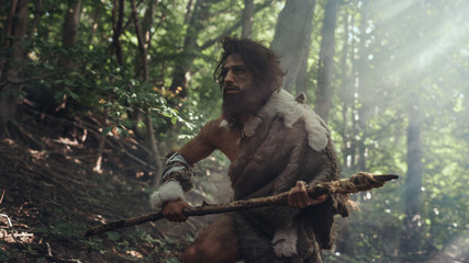 Portrait of Primeval Caveman Wearing Animal Skin and Fur Hunting with a Stone Tipped Spear in the Prehistoric Forest. Prehistoric Neanderthal Hunter Ready to Throw Spear in the Jungle