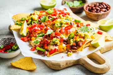 Nachos chips with cheese sauce, guacomole, salsa and vegetables on the board. Party food concept.