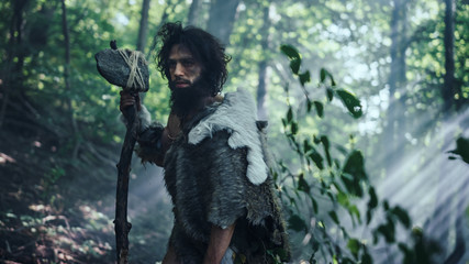 Portrait of Primeval Caveman Wearing Animal Skin and Fur Hunting with a Stone Tipped Hammer in the Prehistoric Forest. Prehistoric Neanderthal Ready to Attack Prey