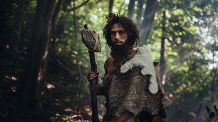 Portrait of Primeval Caveman Wearing Animal Skin and Fur Hunting with a Stone Tipped Hammer in the Prehistoric Forest. Prehistoric Neanderthal Ready to Attack Prey