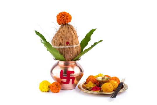Copper Kalash with coconut and mango leaf and pooja thali with diya, kumkum and sweets with floral decoration on a white background. Essential in hindu puja.