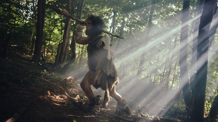 Portrait of Primeval Caveman Wearing Animal Skin and Fur Hunting with a Stone Tipped Spear in the Prehistoric Forest. Primitive Neanderthal Hunter Ready to Throw Spear in the Jungle