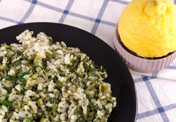Portion of rice with spinach, green onions and a dill with lemon juice on the black plate