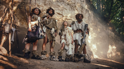 Fototapeta na wymiar Tribe of Four Hunter-Gatherers Wearing Animal Skin Holding Stone Tipped Tools, Pose at the Entrance of their Cave. Portrait of Two Grown Male and Two Female Neanderthals and their Way of Living
