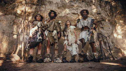 Tribe of Four Hunter-Gatherers Wearing Animal Skin Holding Stone Tipped Tools, Pose at the Entrance...